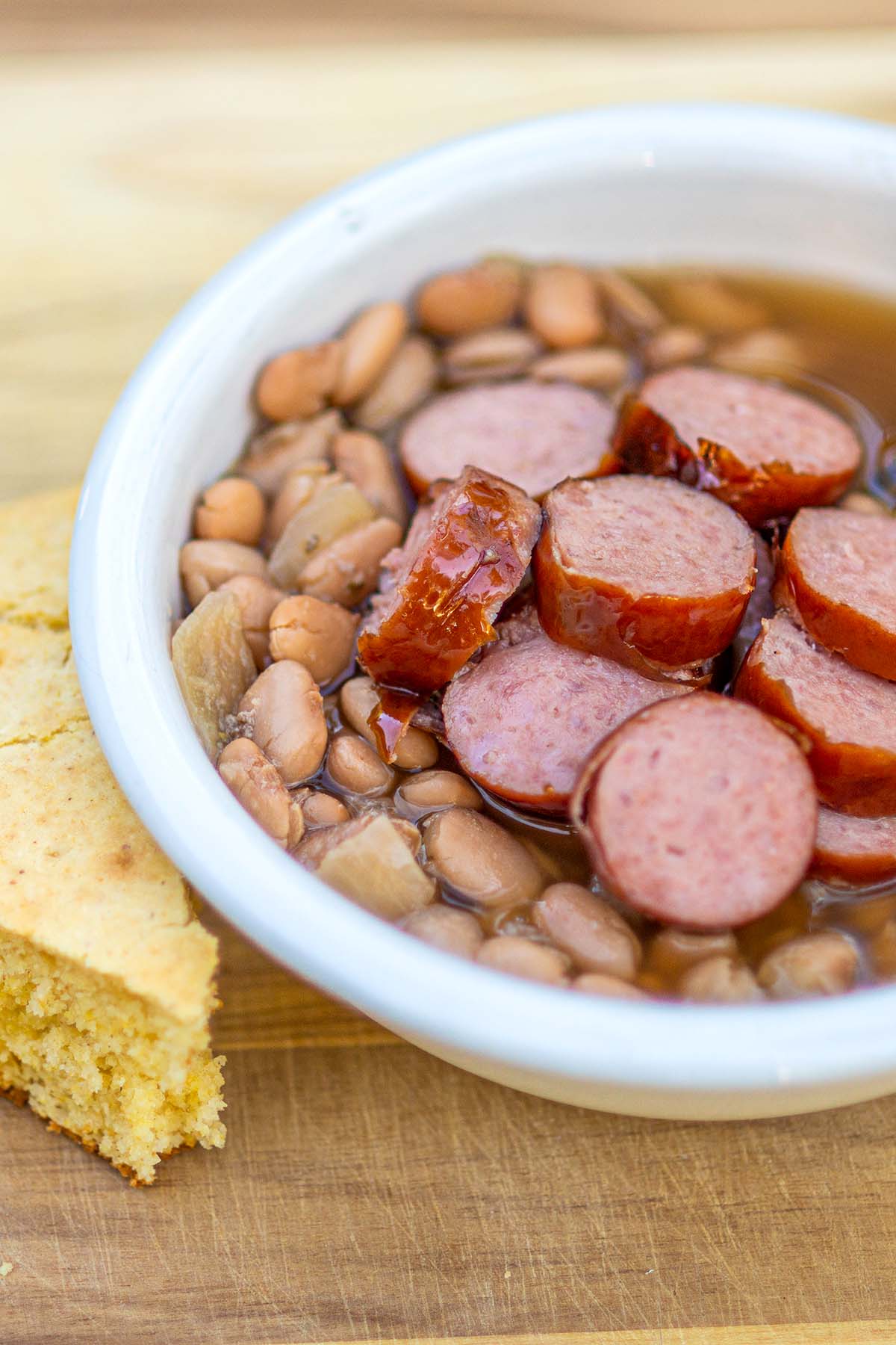 Sausage and bean soup served in a white bowl with a side of corn bread.