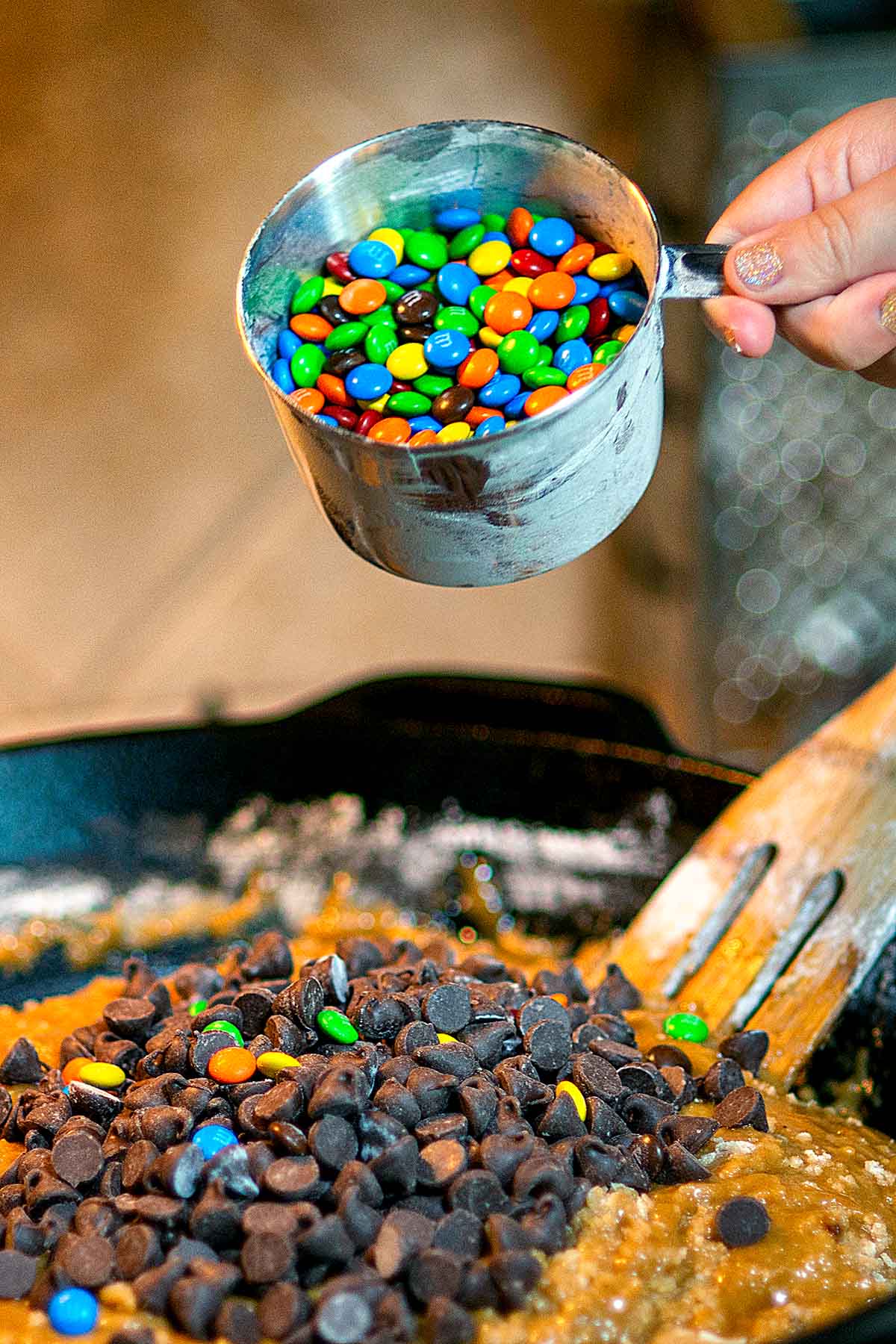 M&M's being poured into a cast iron skillet full of cookie dough.