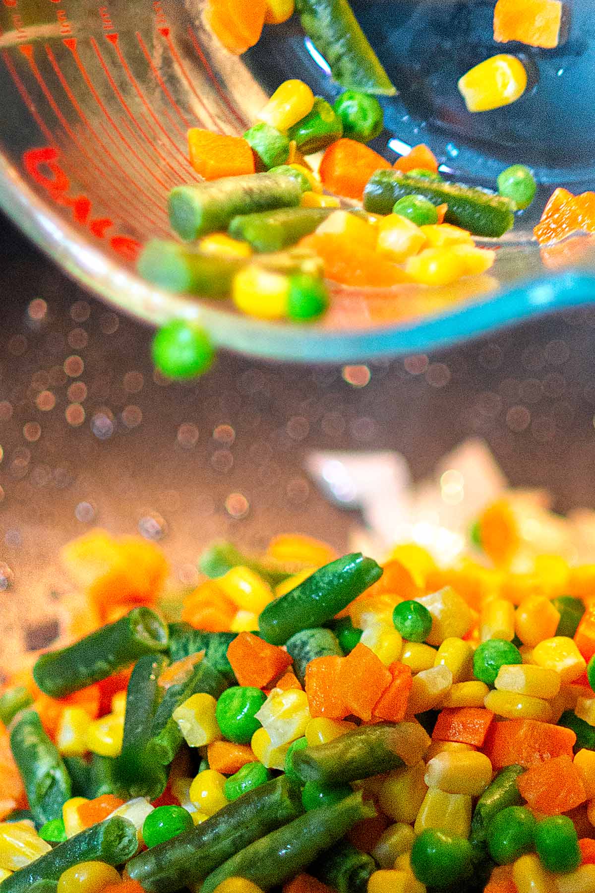 Mixed vegetables are poured into a wok.