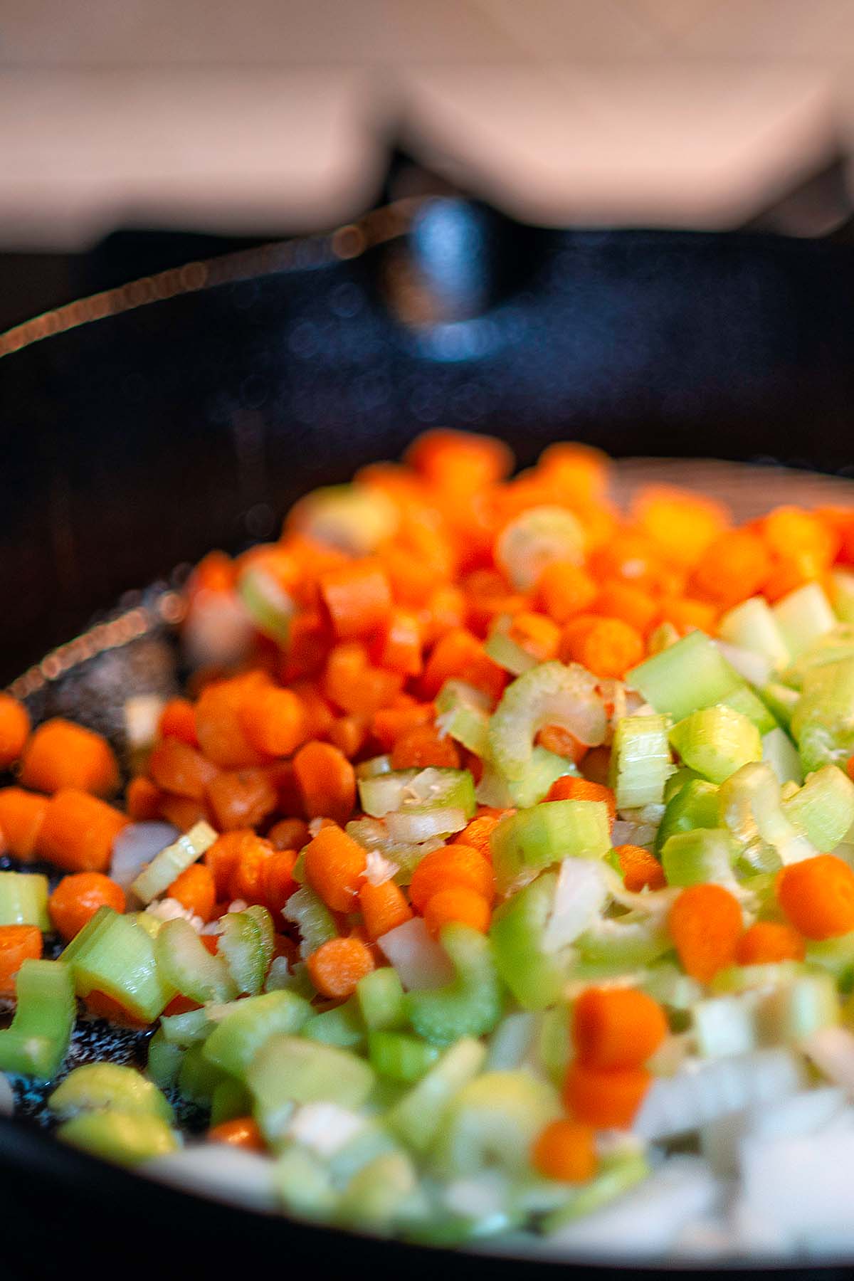 Carrots, celery, and onions being sautéd in a cast iron skillet.