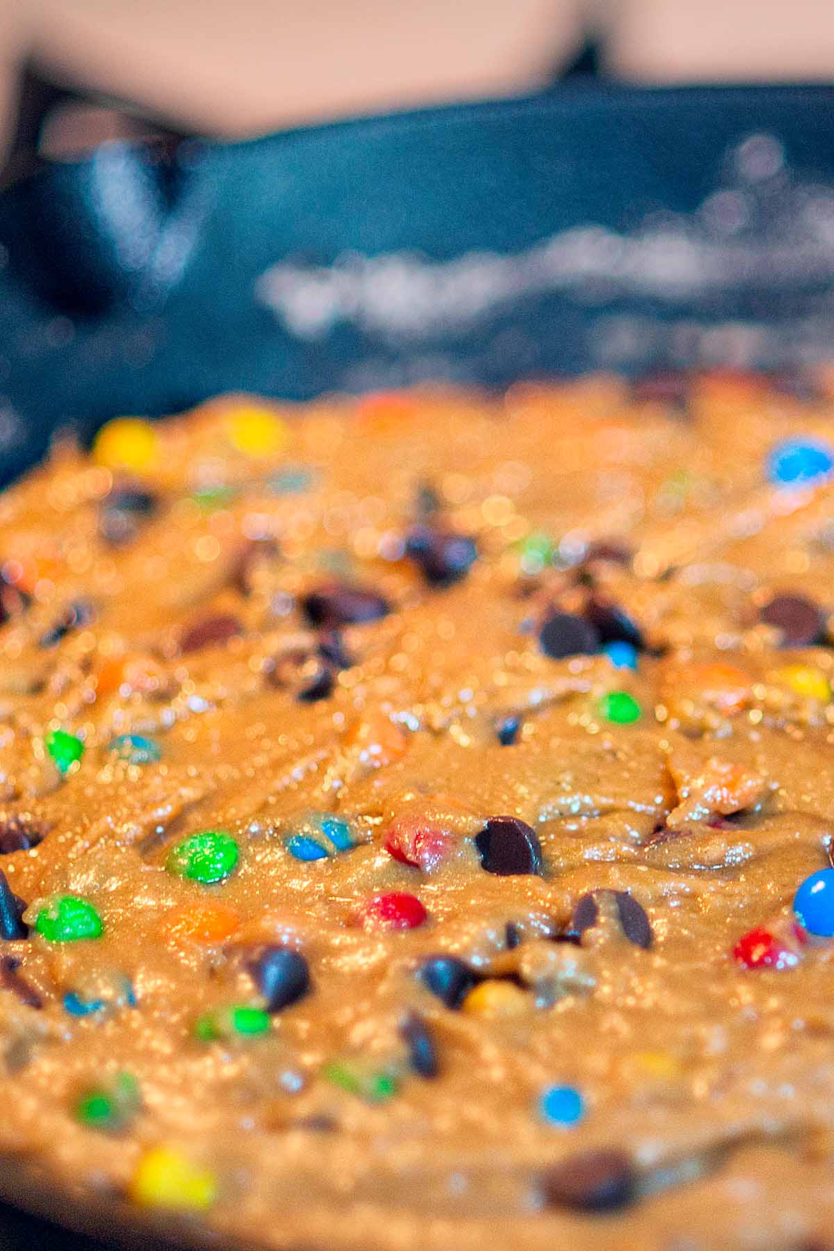 M&M and chocolate chip cookie dough spread evenly through a large cast iron skillet.