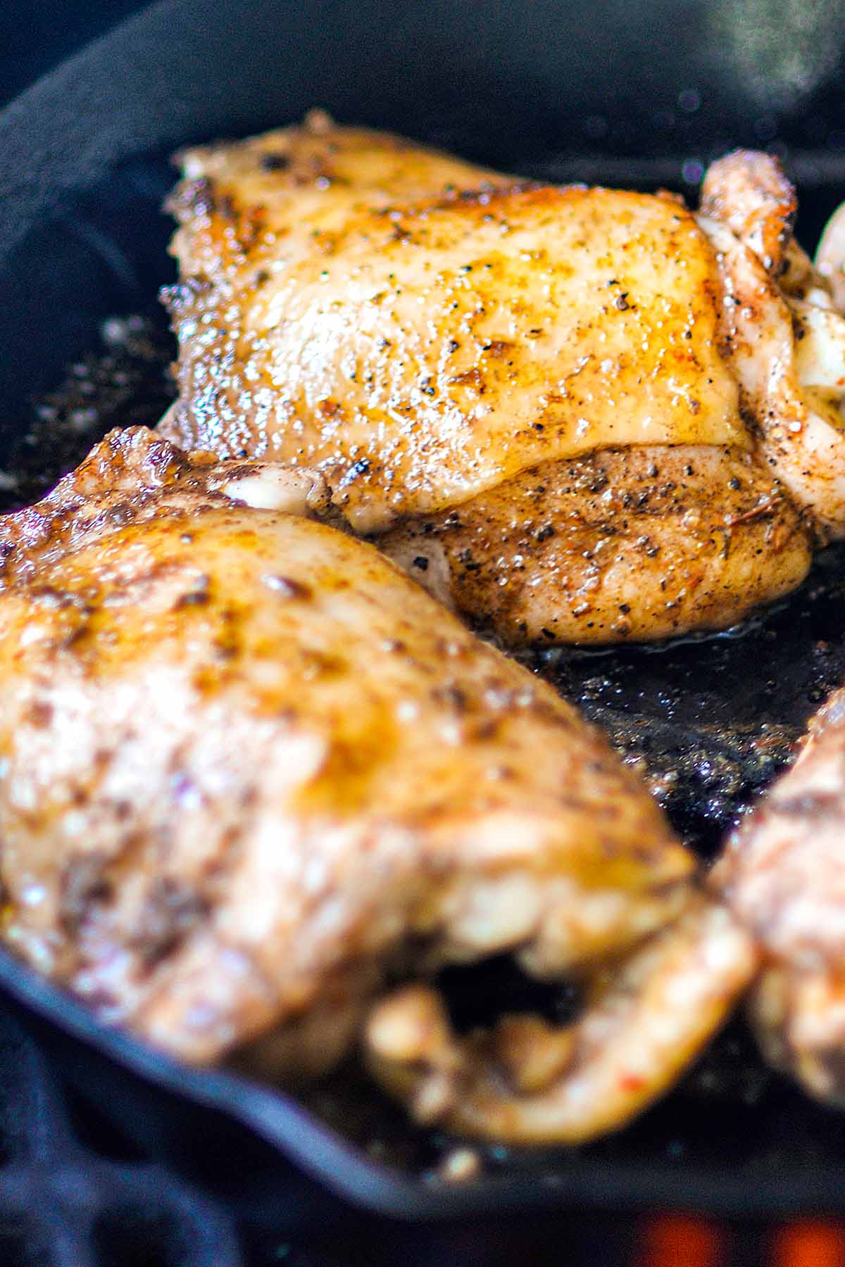 Jerk Chicken thighs cooking in a cast iron skillet on the grill.