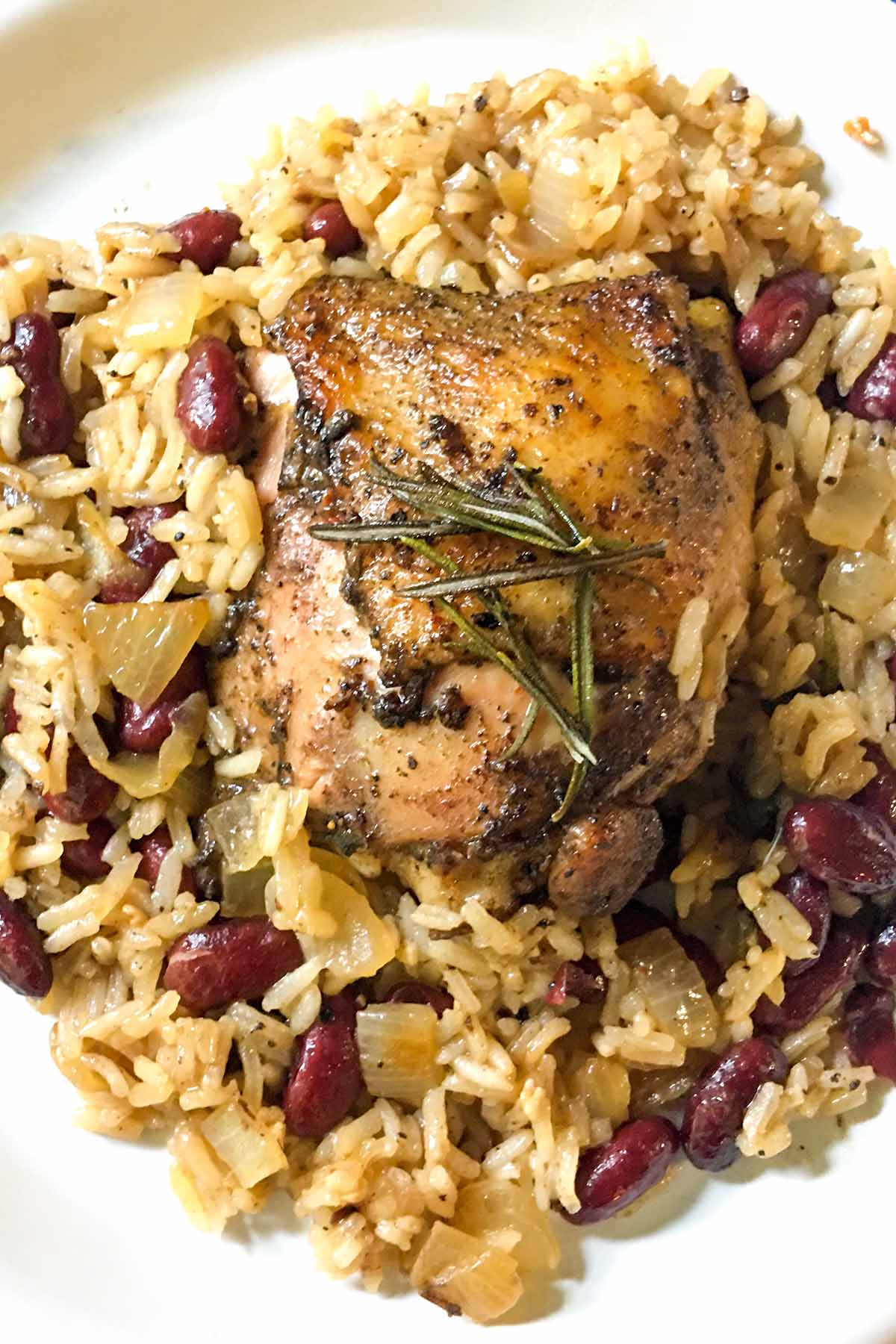 Jerk Chicken with coconut rice and red beans served on a white plate.