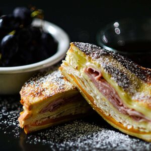 Monte Cristo Sandwich sliced and served with powdered sugar grapes and maple syrup.