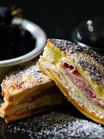 Monte Cristo Sandwich sliced and served with powdered sugar grapes and maple syrup.