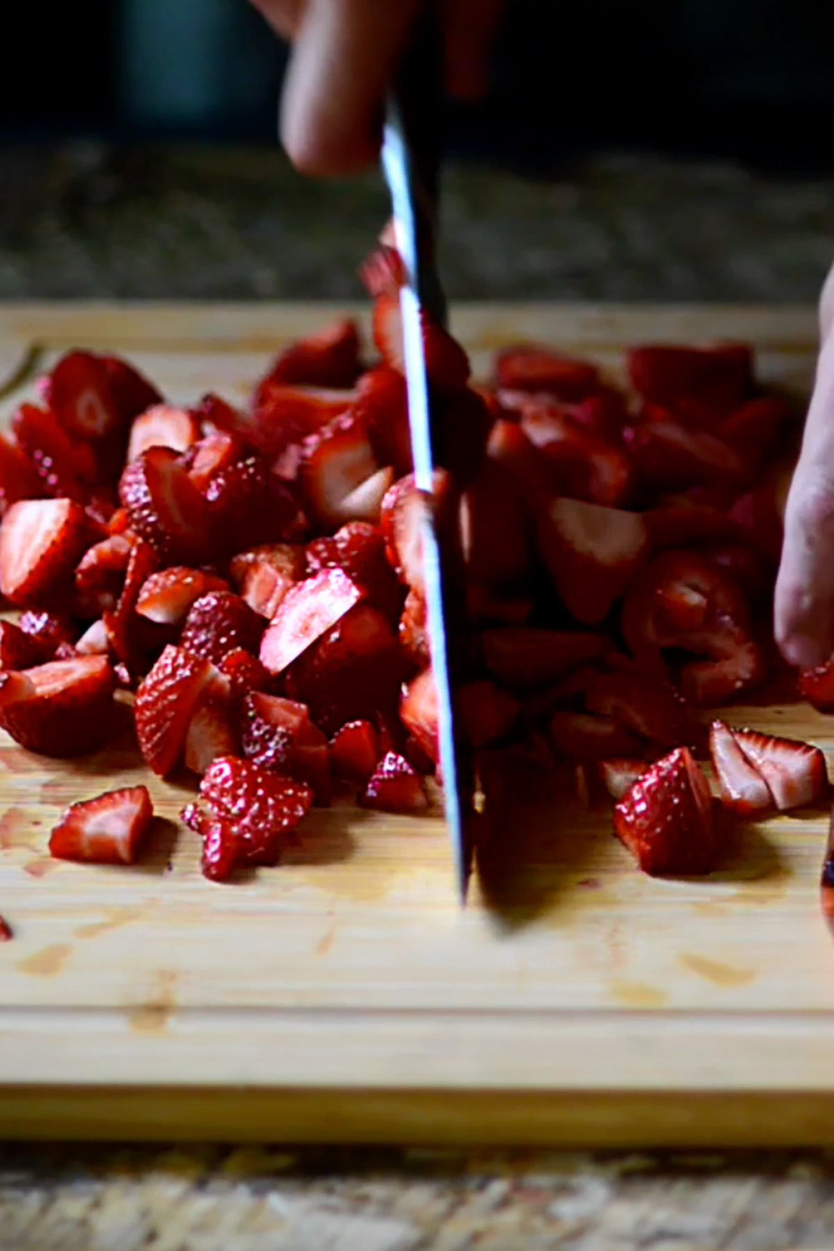 Strawberries being sliced on a wood cutting board.