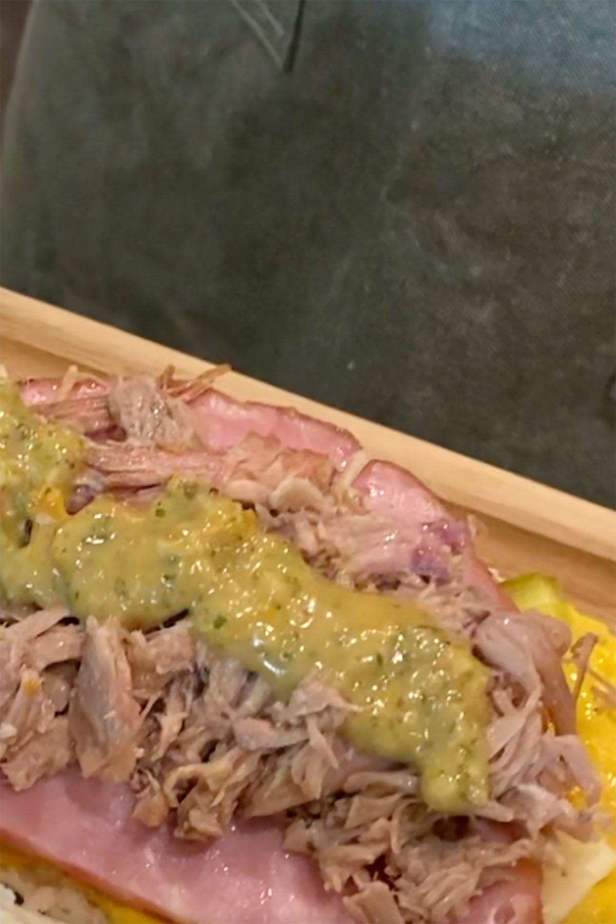 A sandwich with mustard, ham, cheese, pulled pork, and mojo sauce.