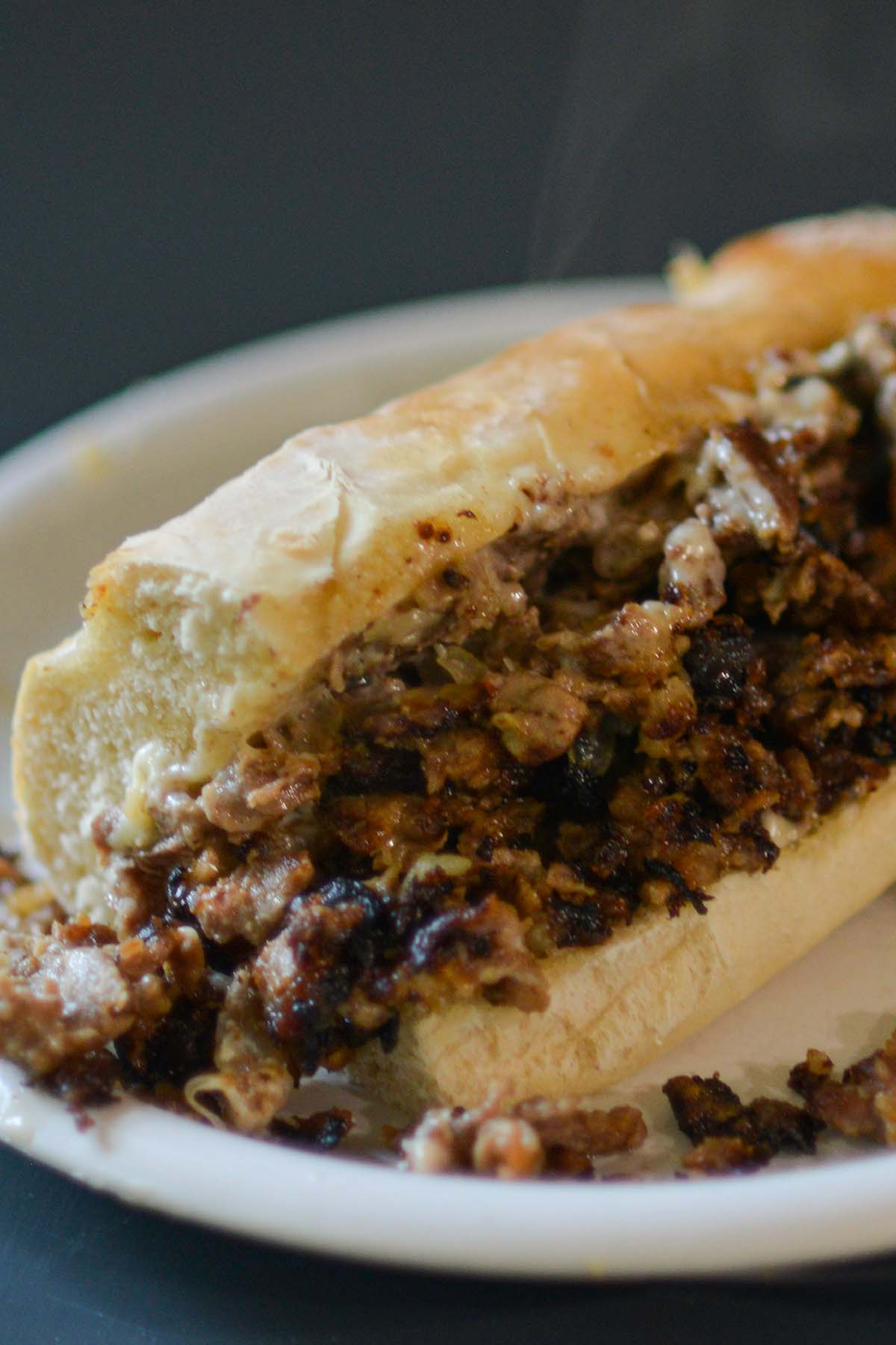 Philly cheesesteak sandwich served on a white plate. 