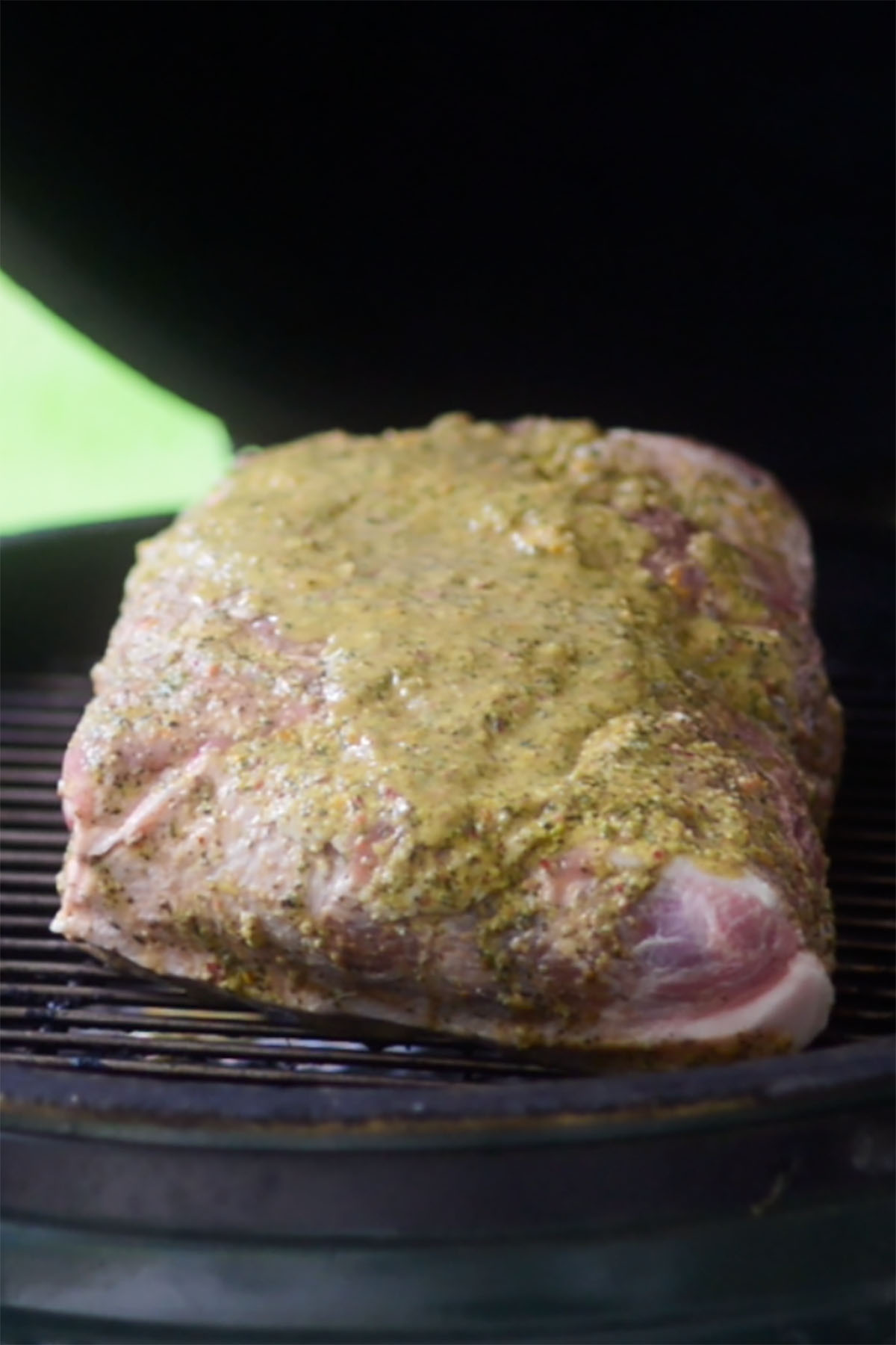 A pork butt shoulder on the grate of a big green egg with mojo sauce poured over the top.