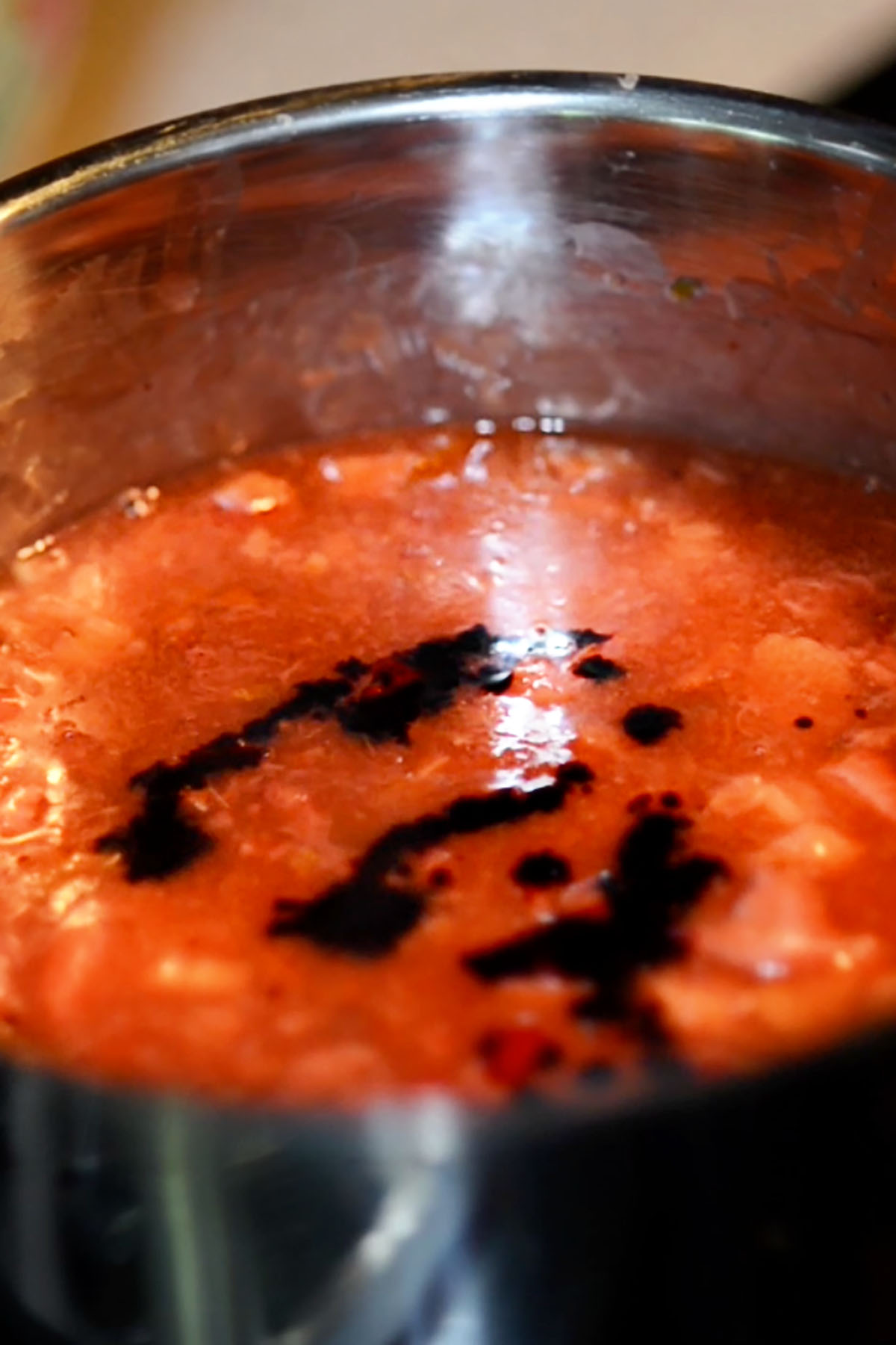 Red food coloring added to a strawberry rhubarb mixture in a sauce pan.