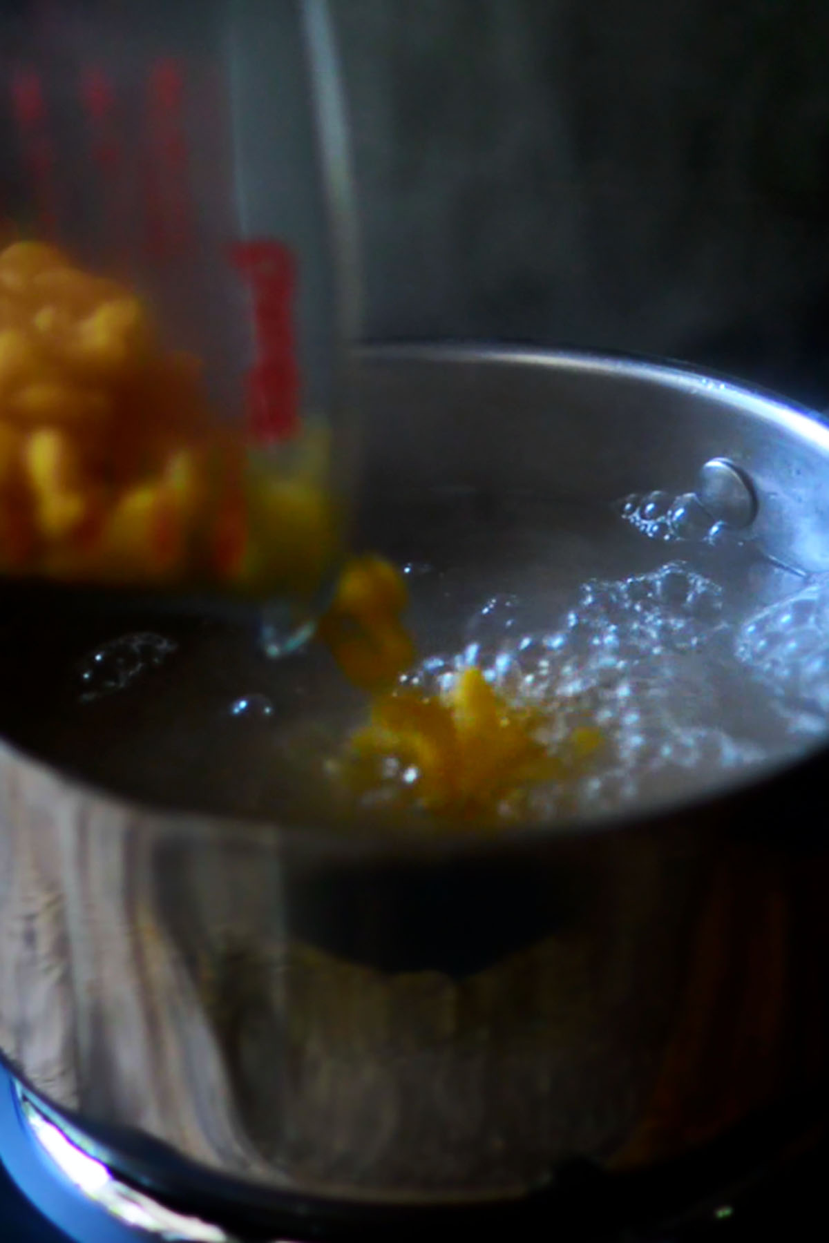 Elbow macaroni being poured into a stock pot of boiling water.