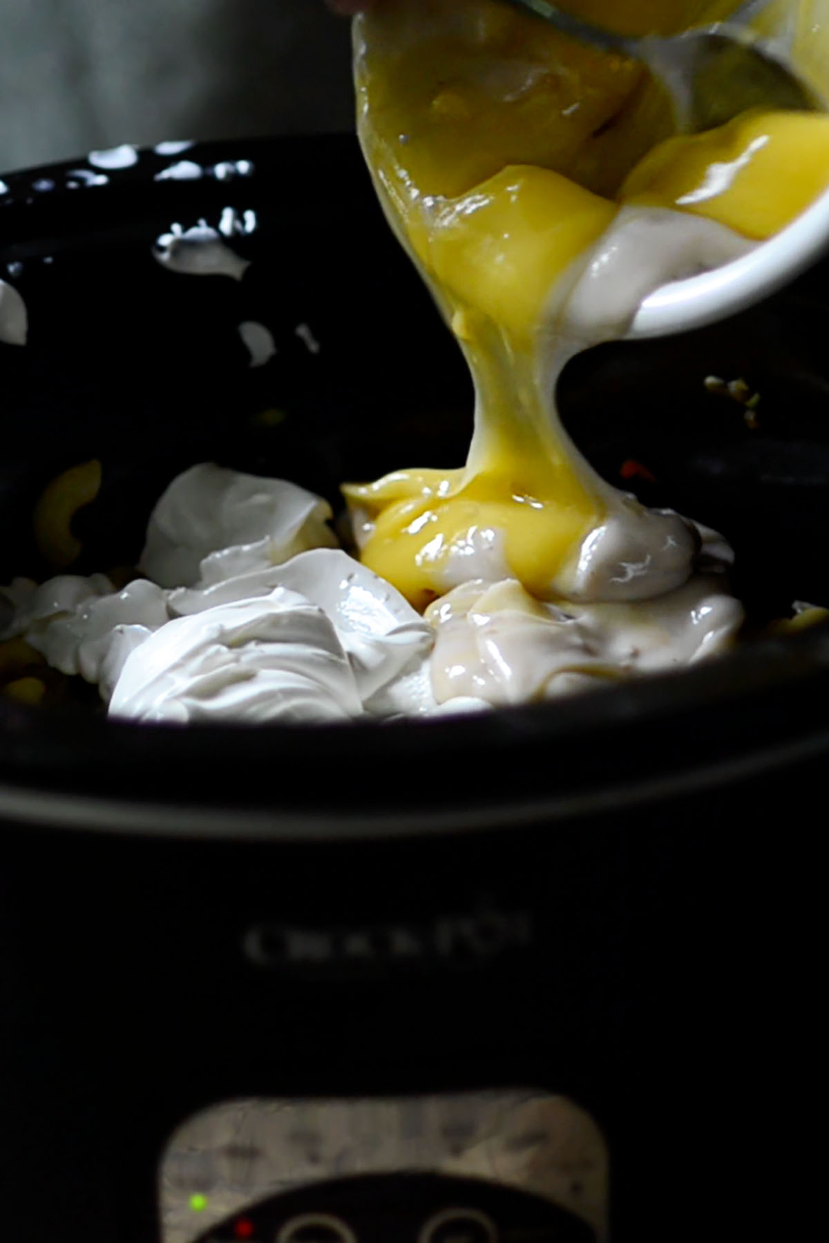Sour cream and cream of mushroom soup being poured into a crock pot.