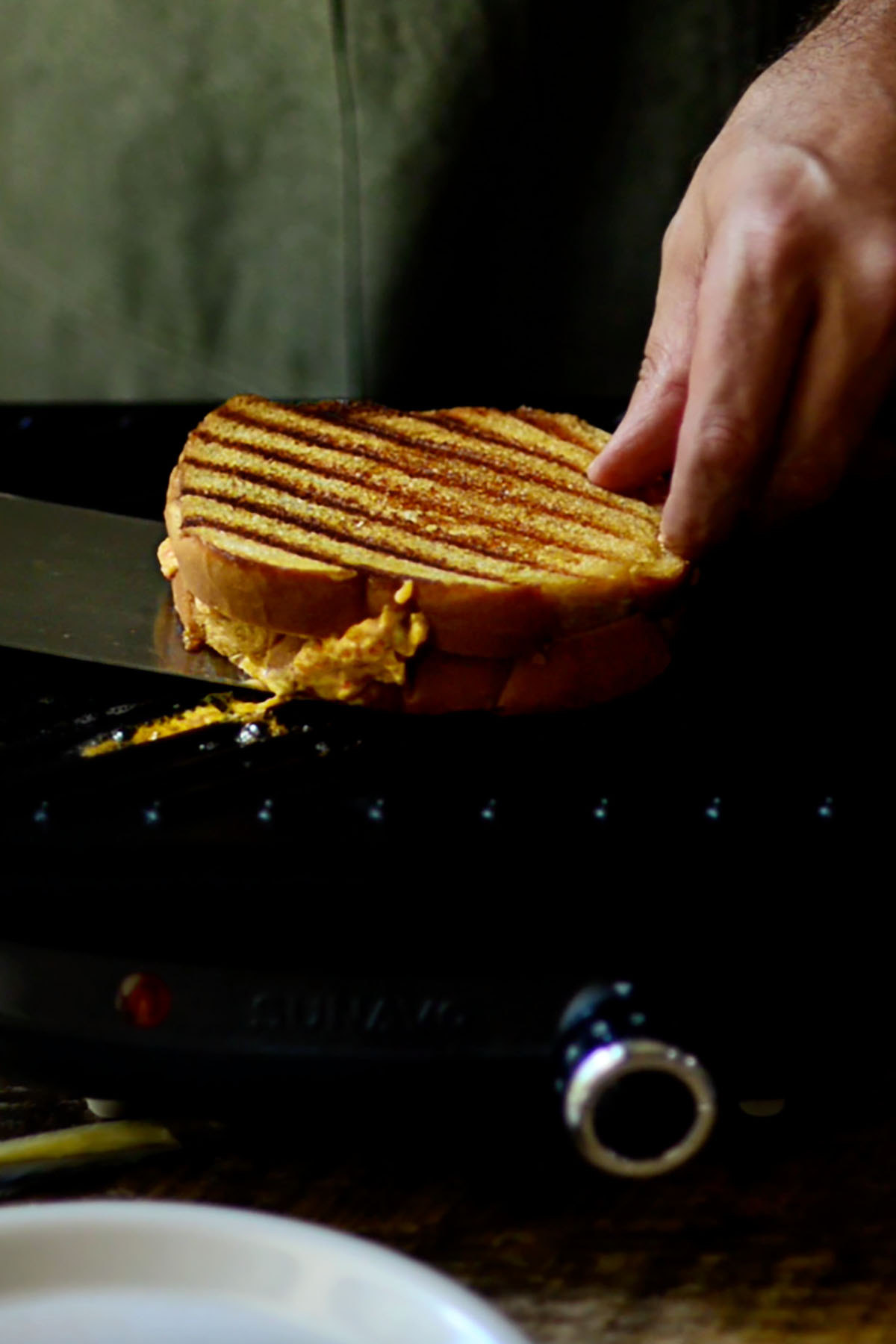 A grilled cheese sandwich being flipped over on a cast iron griddle showing the grill marks.