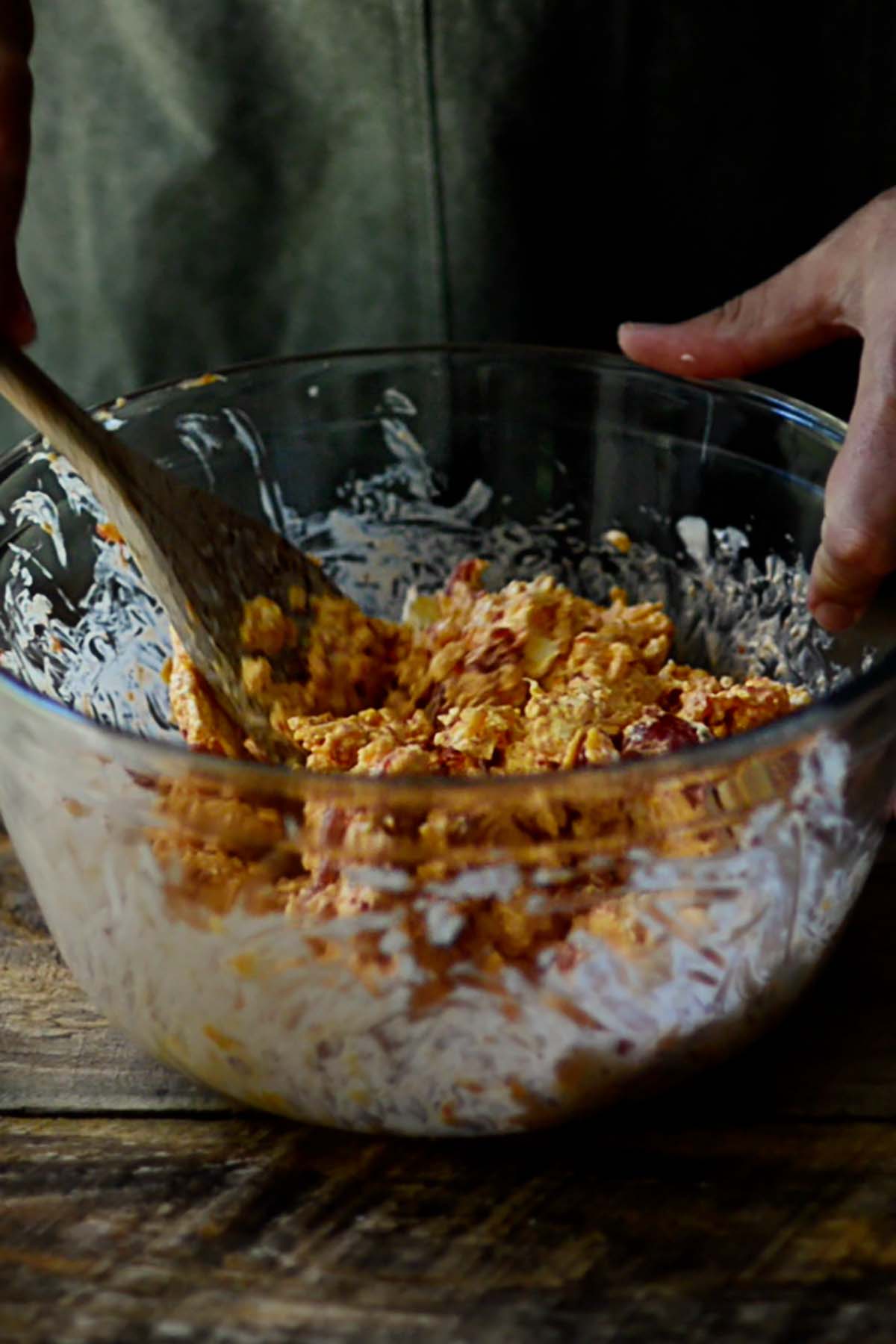 Pimento cheese being mixed in a large glass mixing bowl.