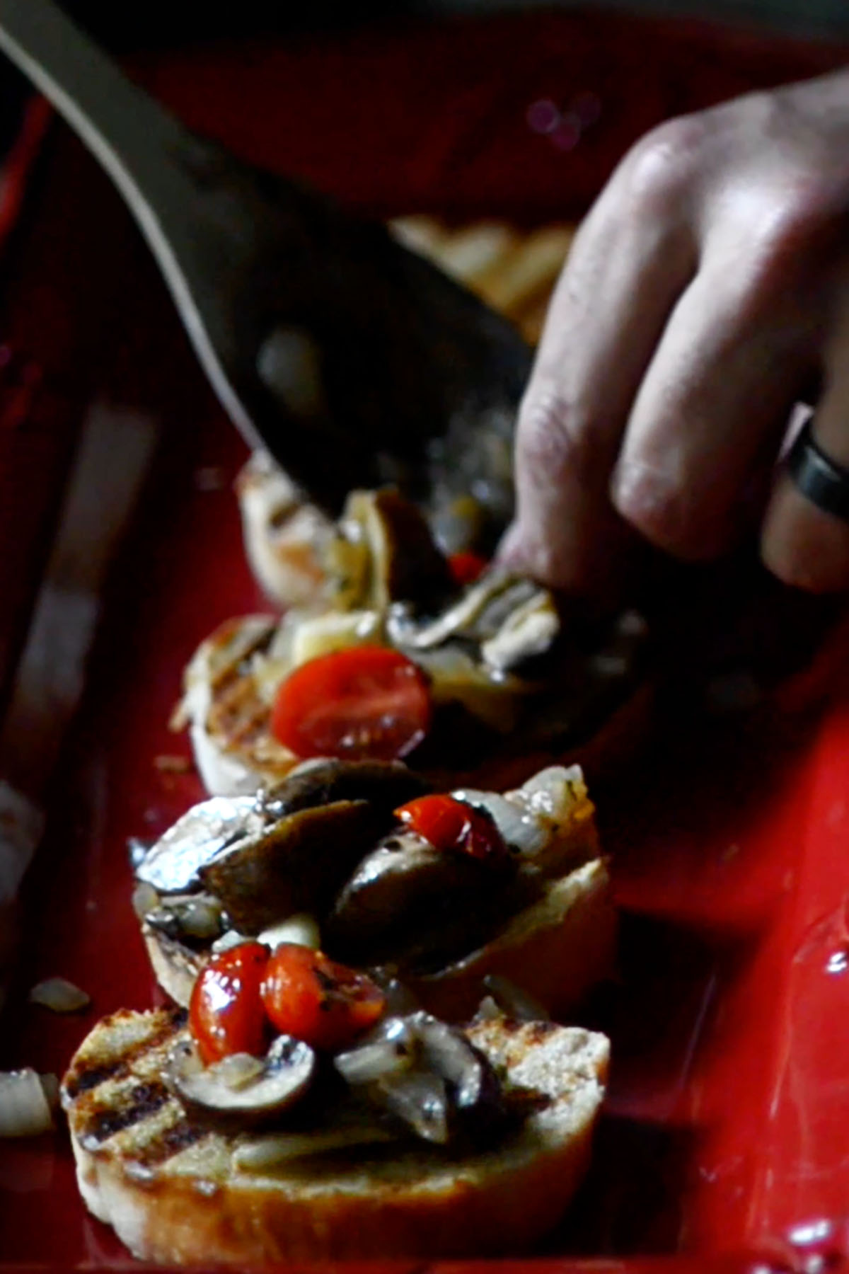Sliced and toasted baguette being topped with roasted tomatoes, mushrooms, and onions.