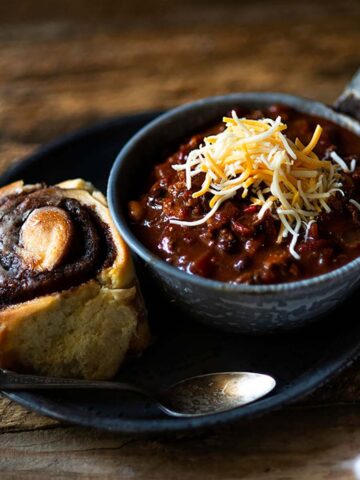 Crock pot chili served in a bowl with a cinnamon roll and crackers on the side.