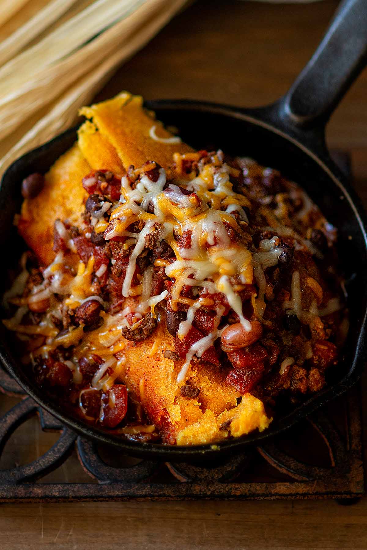 Mississippi Delta Hot Tamales topped with homemade chili and shredded cheese served in a small cast iron skillet.