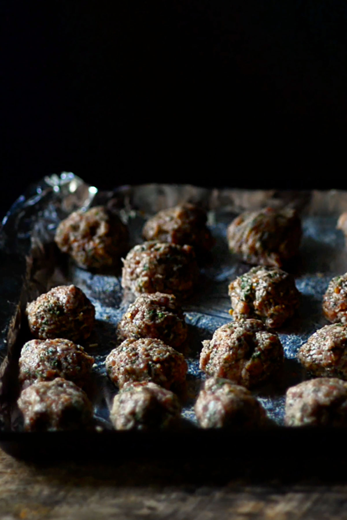 Meatballs formed and uniformly spaced on a foil lined baking sheet.