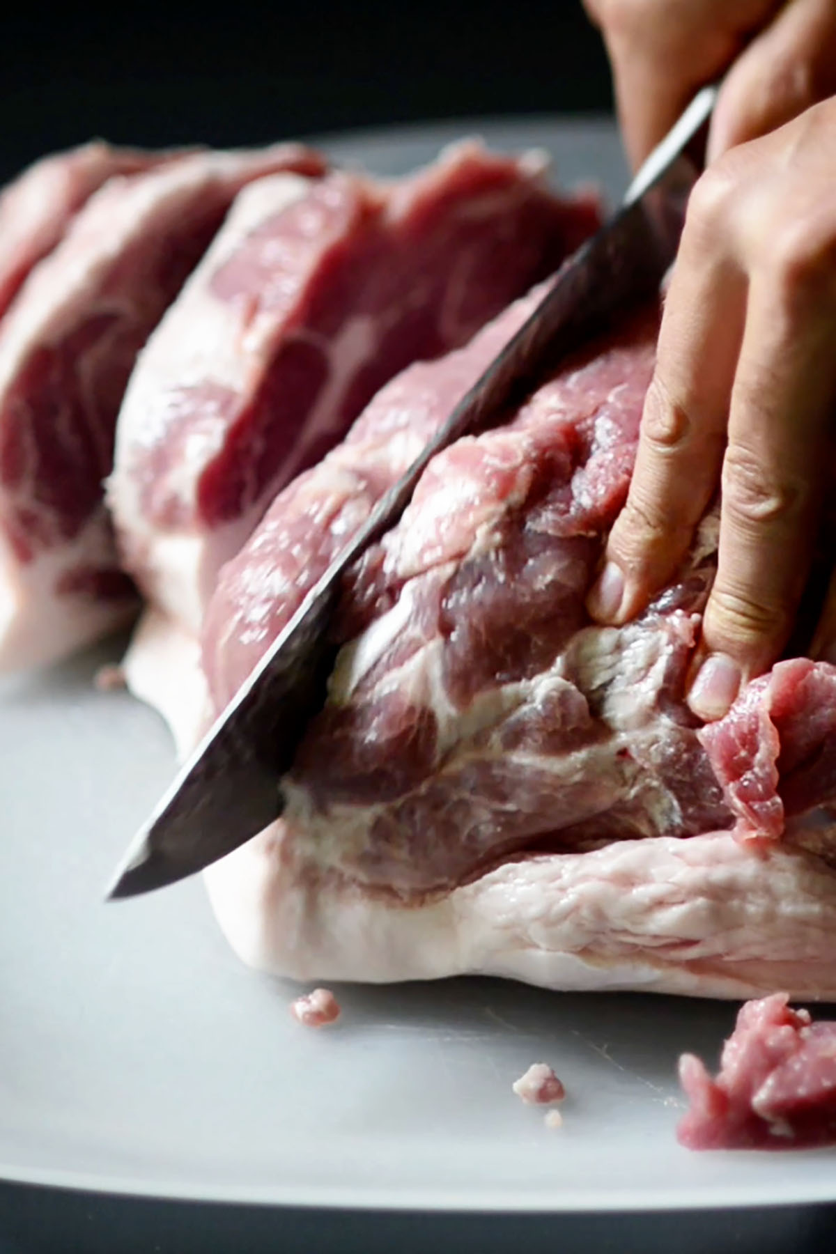 Pork shoulder being sliced into strips.