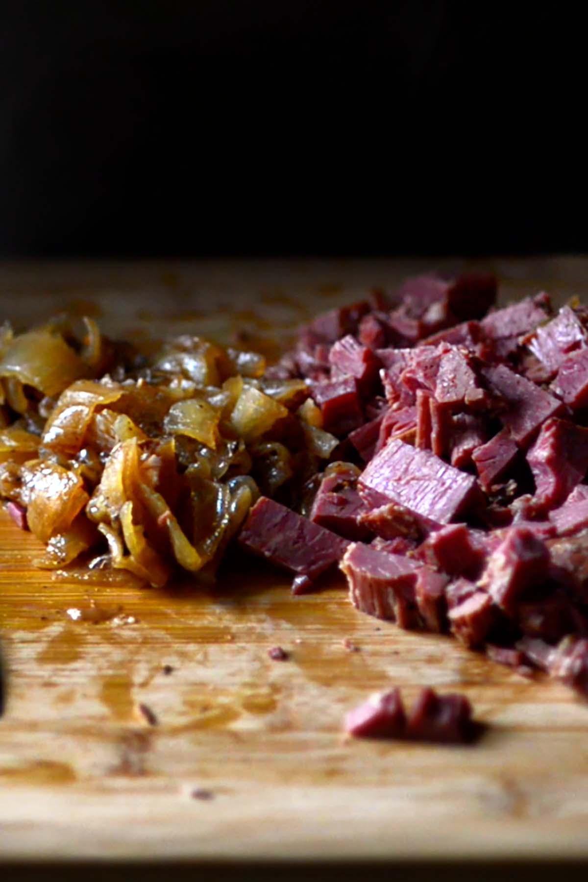 Cooked corned beef brisket and onions chopped on a wooden cutting board.