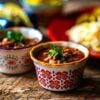 Two bowls of charro beans with tacos and toppings blurred in the background.