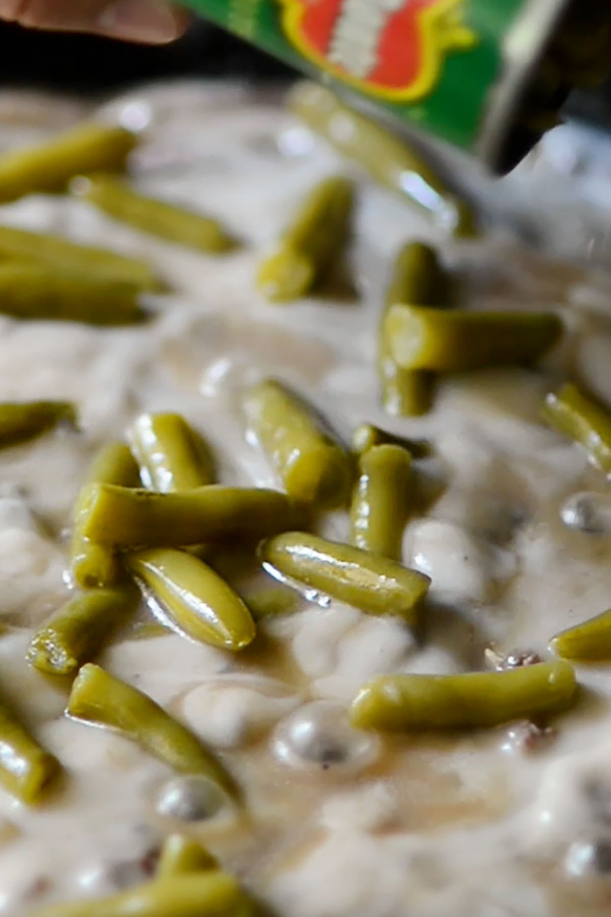Canned green beans being poured over cream of mushroom soup.