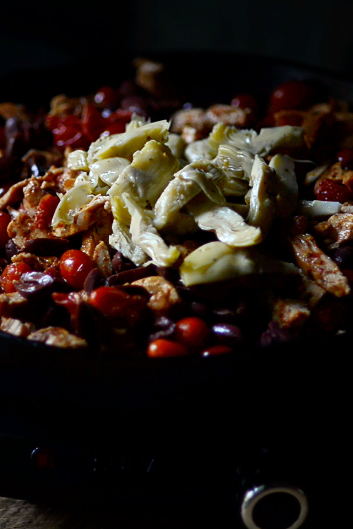 Kalamata olives and artichoke hearts added to cast iron skillet with tomatoes and onions.