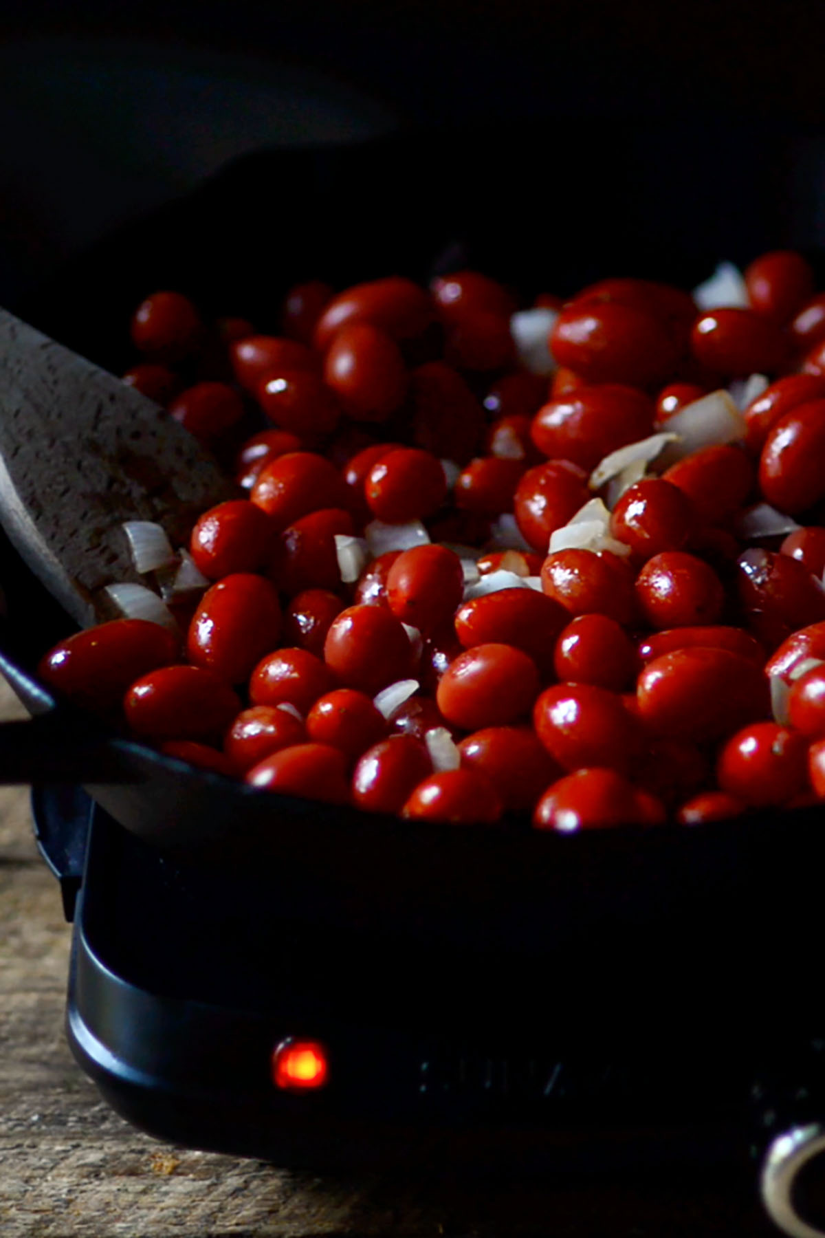 Whole cherry tomatoes and onions cooking in a cast iron skillet.