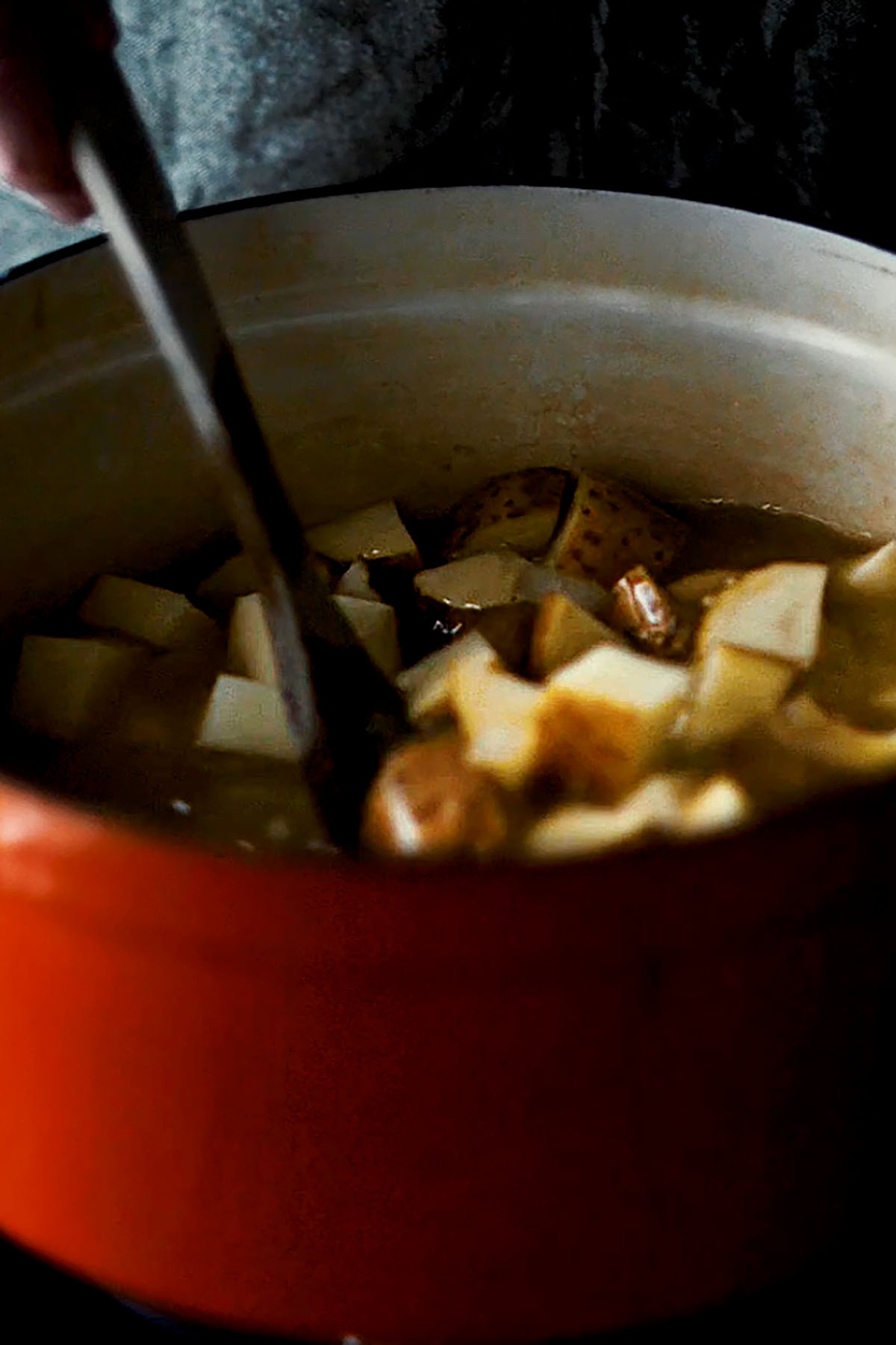 Cubed potatoes being stirred in a soup.
