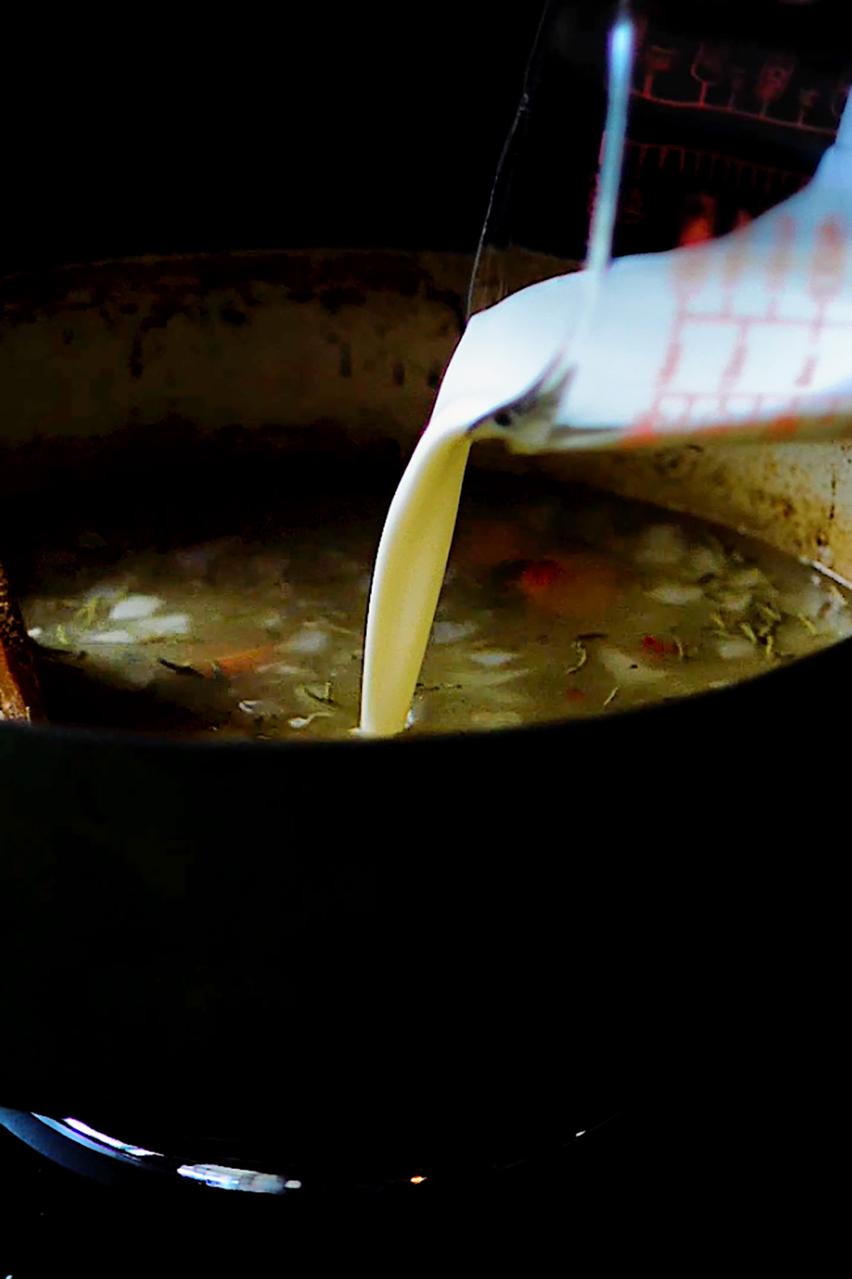 Cream being added to chicken soup in a dutch oven.