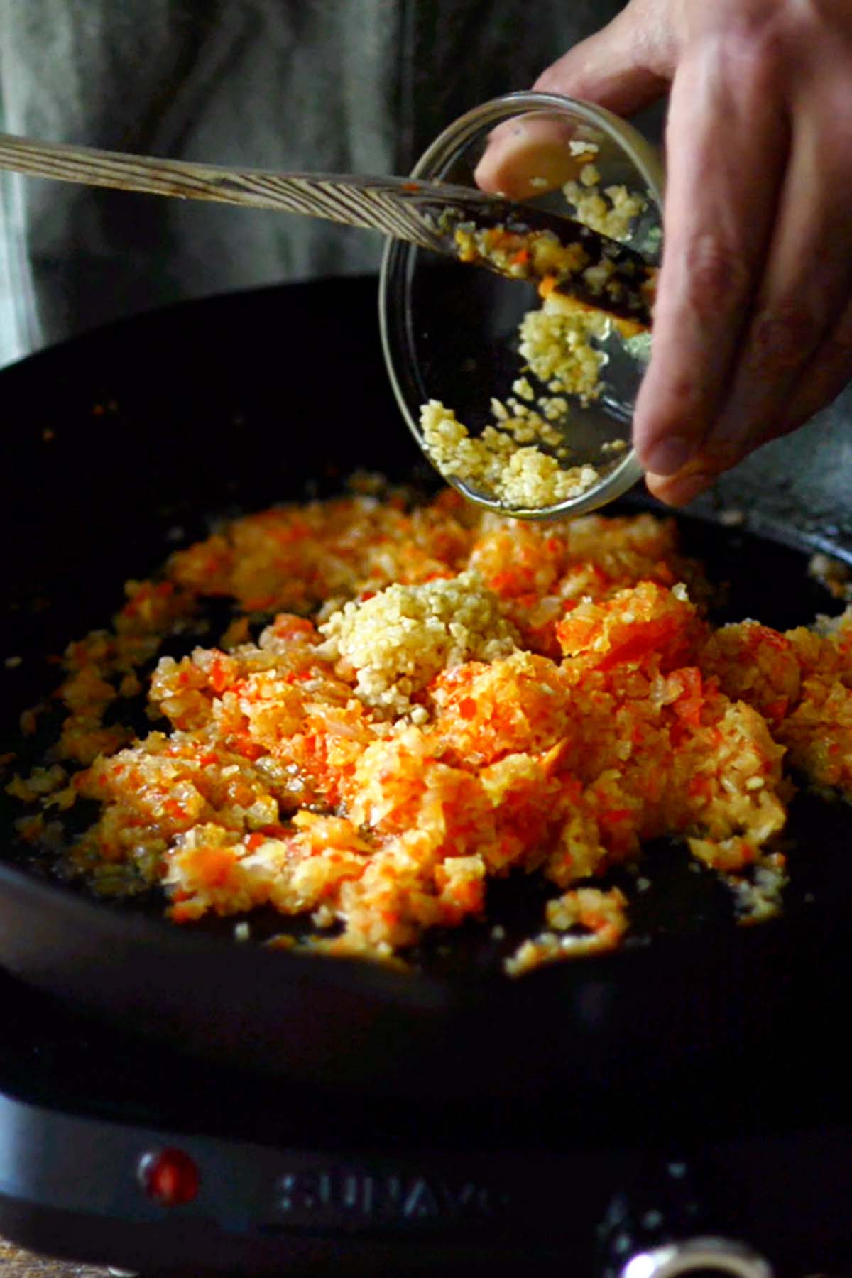 Minced vegetables and garlic being added to a cast iron skillet.