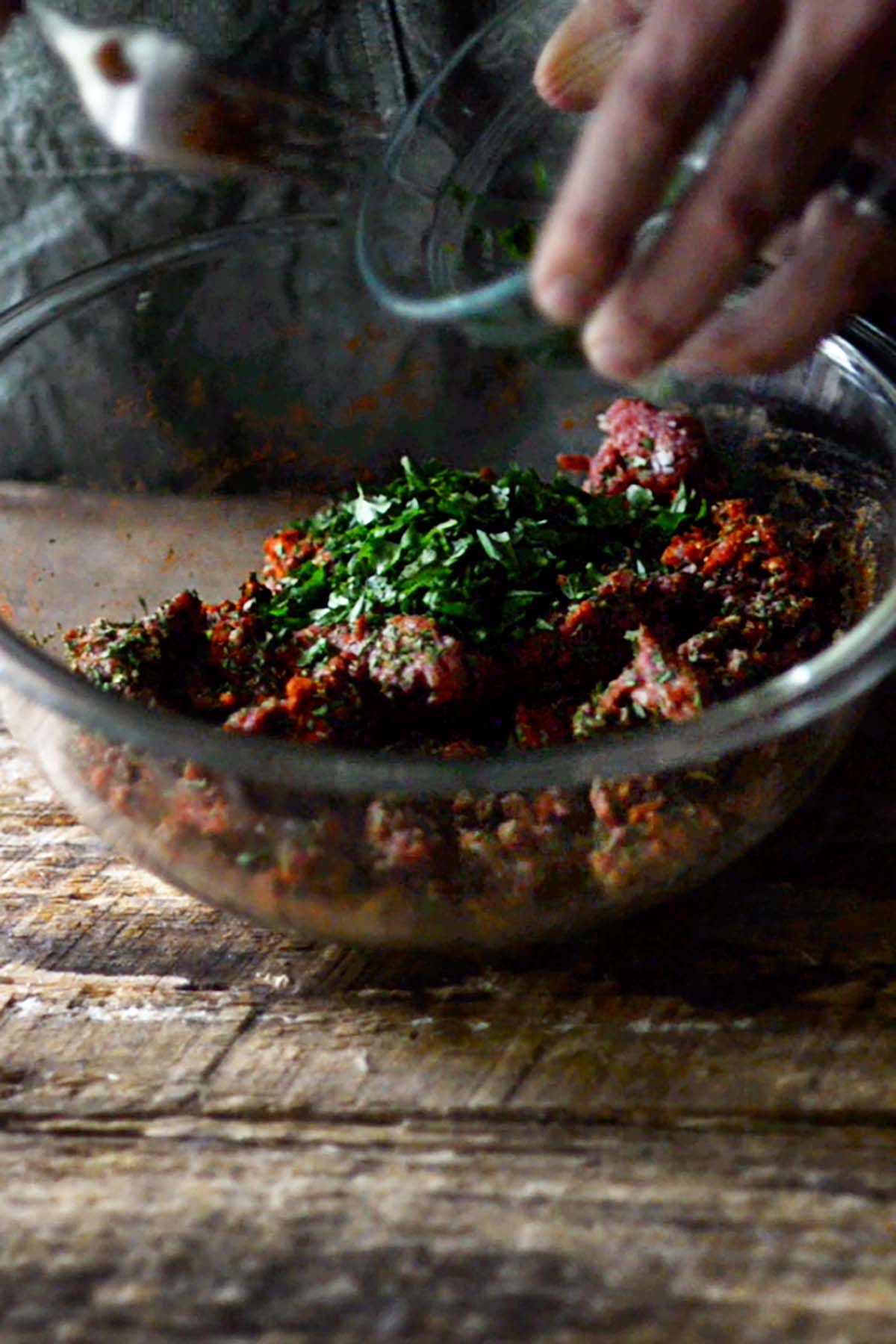 Ground beef, herbs, and spices in a glass mixing bowl.