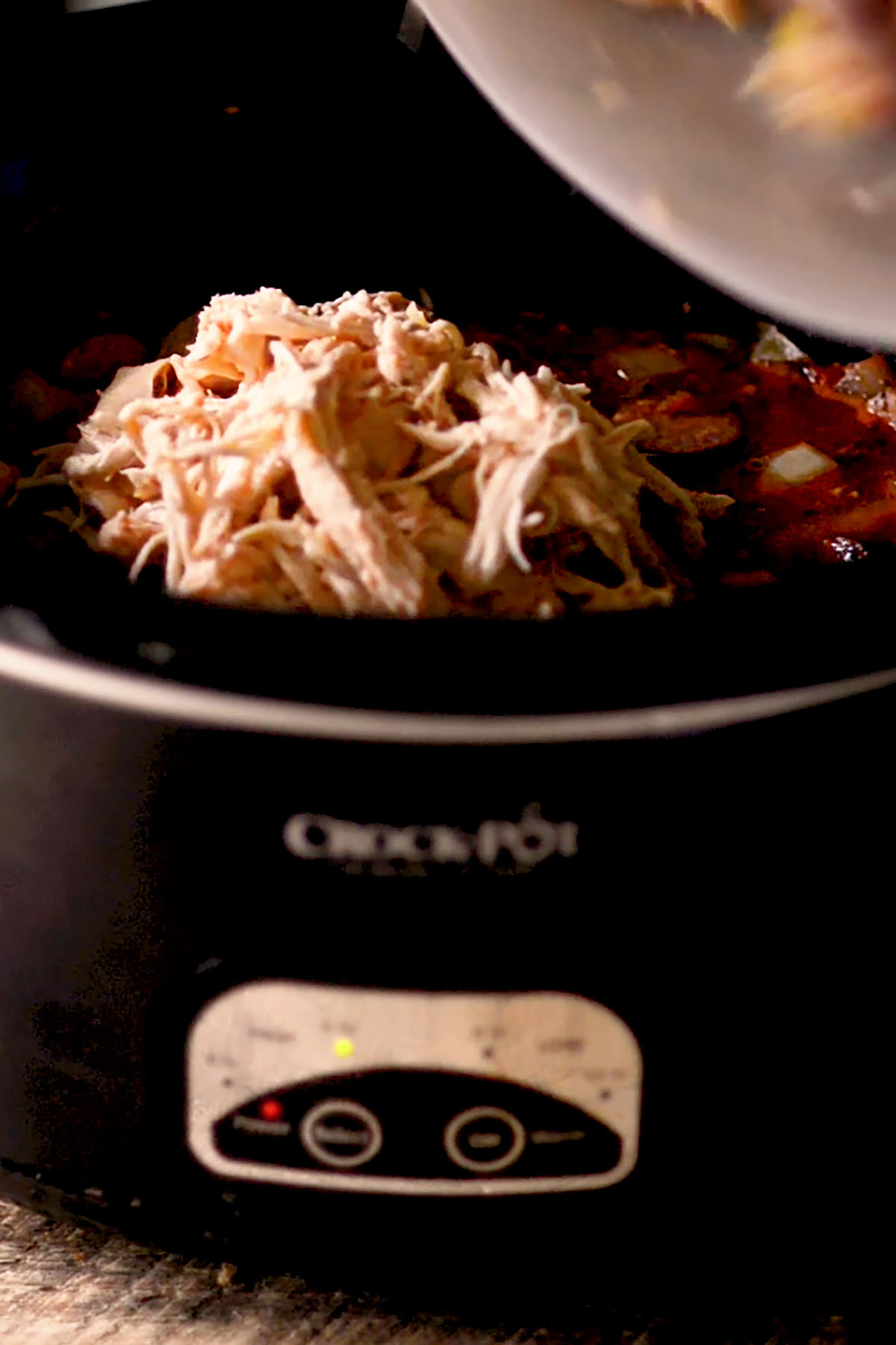 Shredded chicken being added to a Crock Pot.