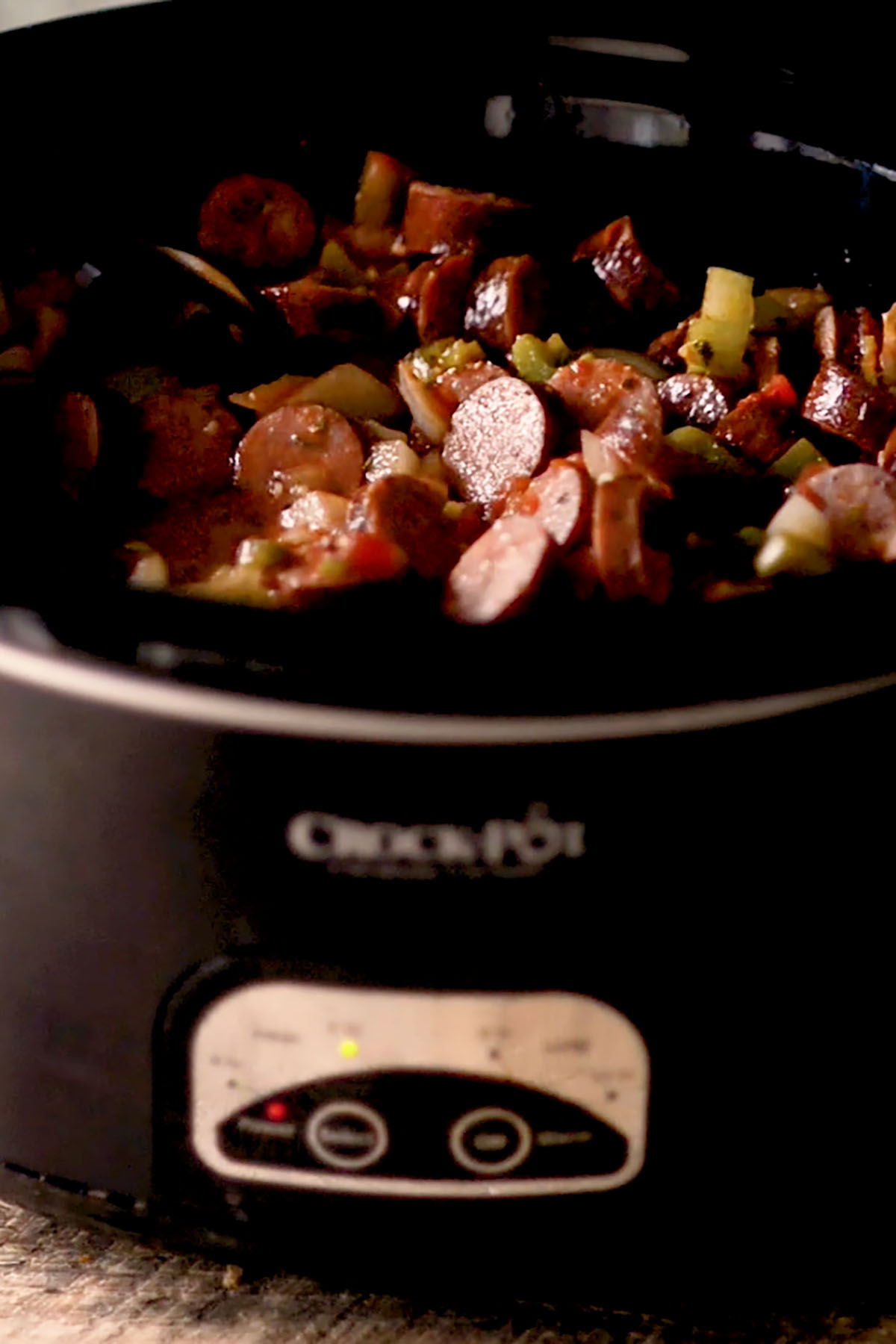 A crock pot full of sliced smoked sausage, chicken breasts, diced vegetables, and tomato sauce.