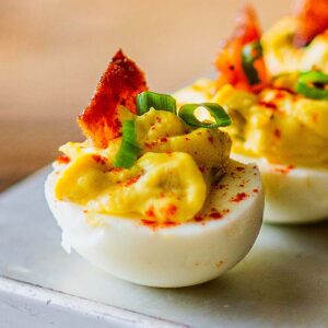 Jalapeño Deviled eggs with candied bacon served on a metal platter.