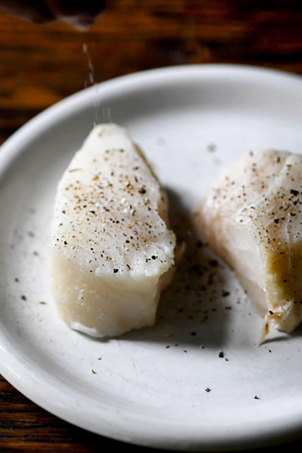 Two Chilean Sea Bass steaks on a plate with salt and pepper.