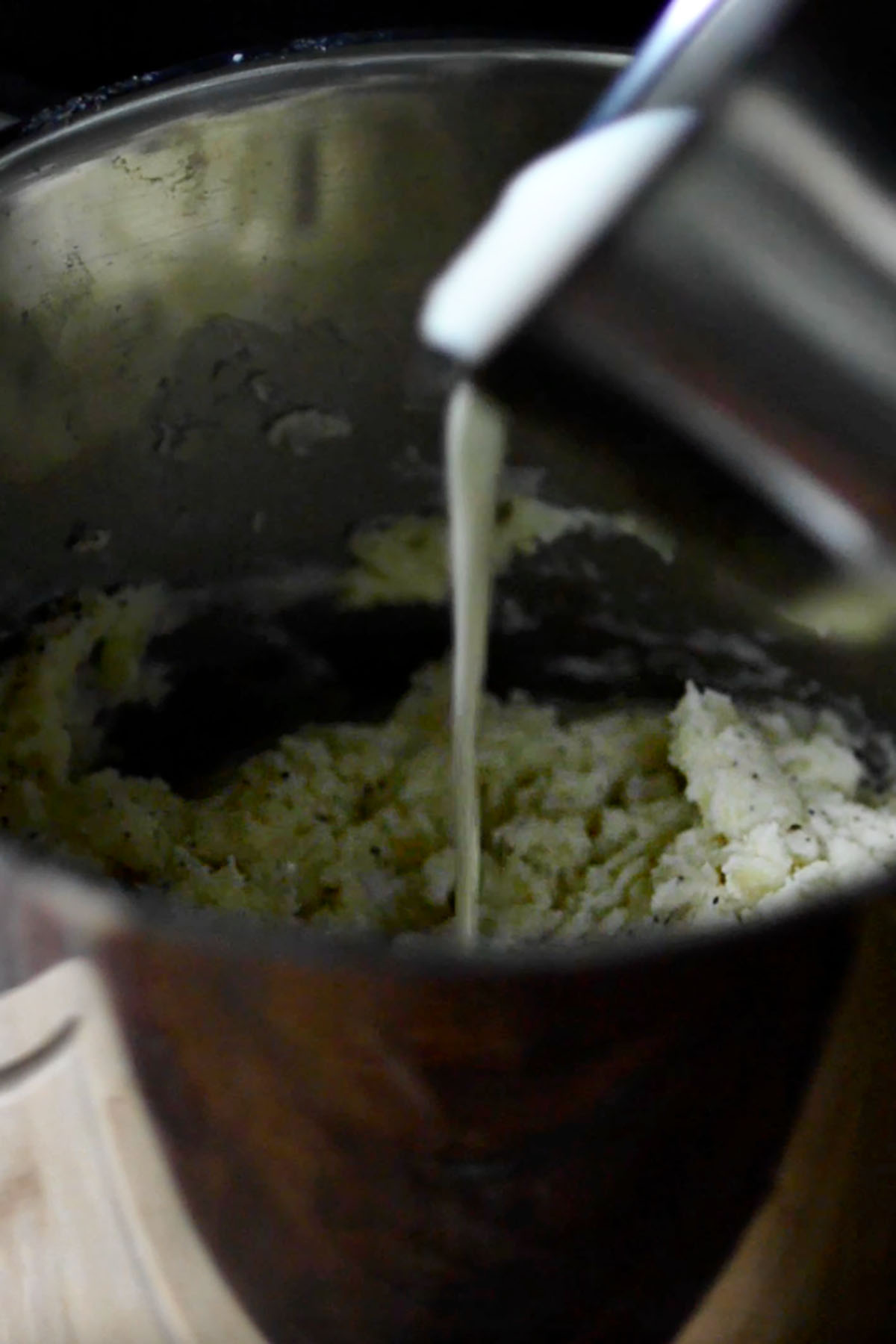 Garlic infused cream being poured into a mashed potato mixture.