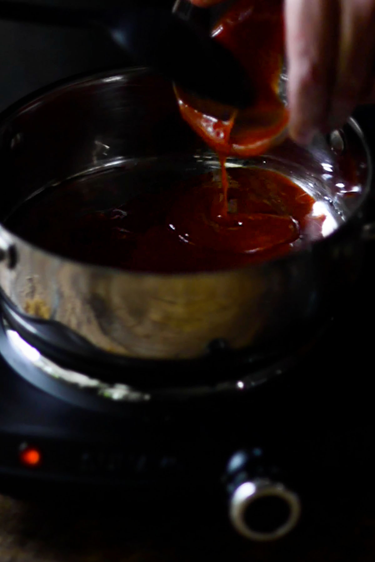 Ketchup being added to a small sauce pan over a heating element.