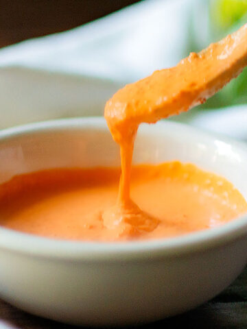 Roasted Red Pepper Sauce in a white bowl with a spoonful pouring the sauce into the bowl.