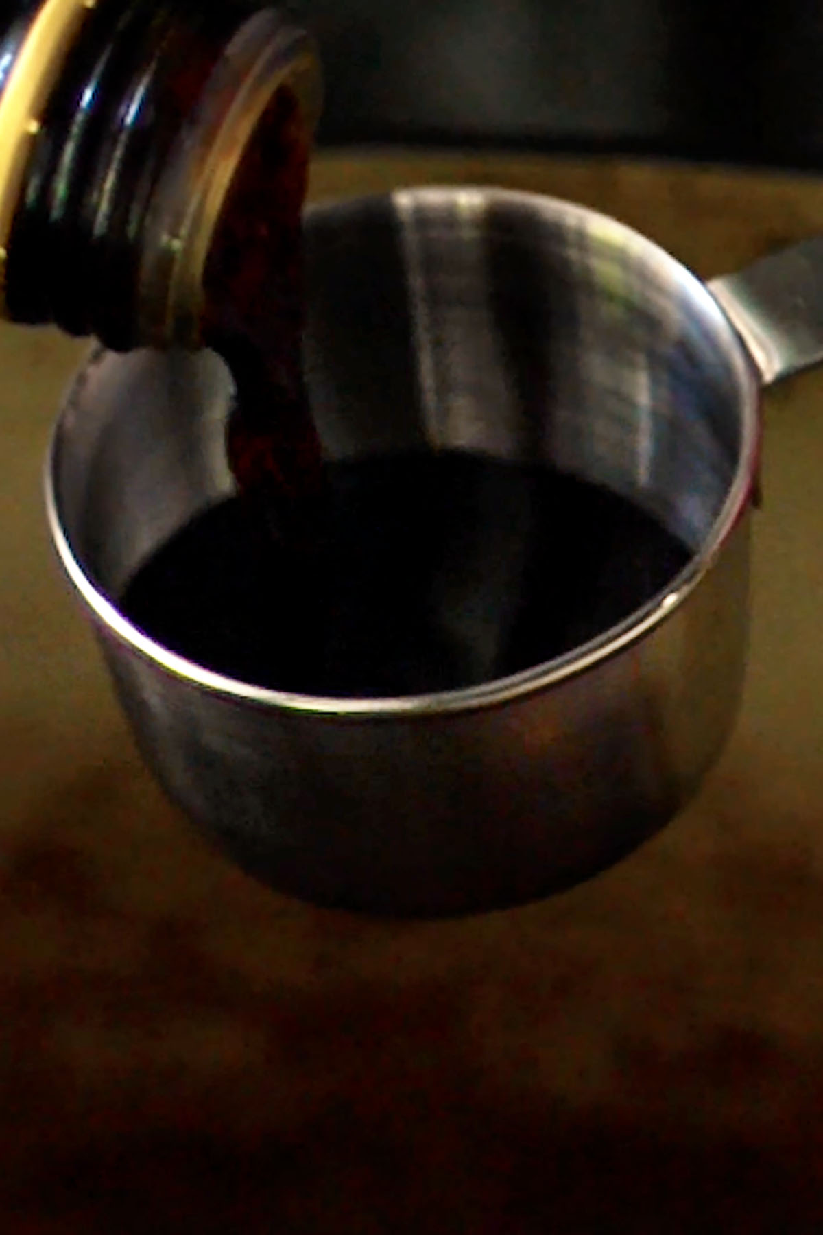 Balsamic vinegar being measured in a metal measuring cup. 