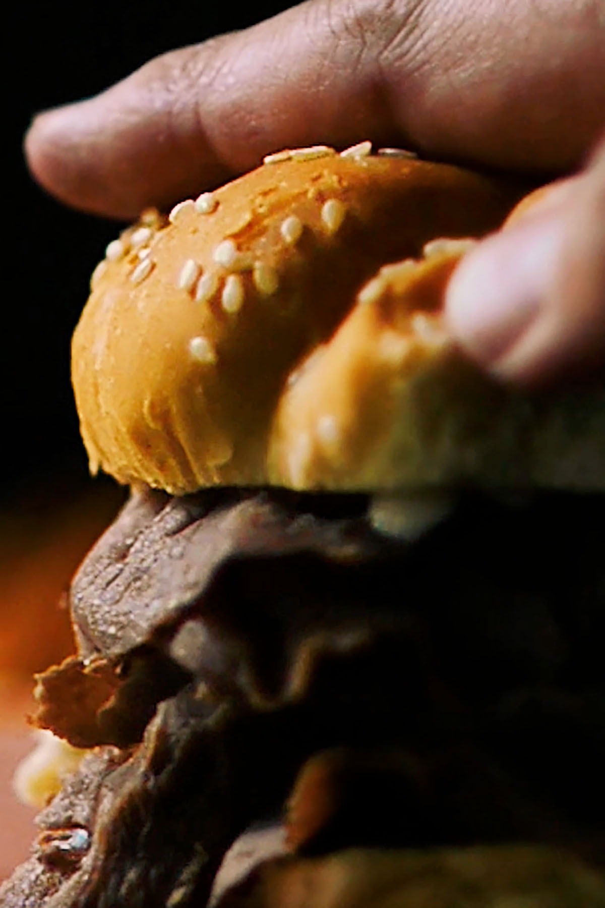 A sesame seed split top bun being pressed down onto a roast beef sandwich.
