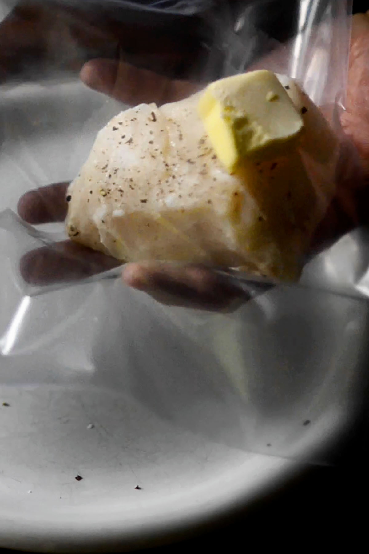 A chilean sea bass steak being placed in a vacuum seal bag with a pat of butter on top.