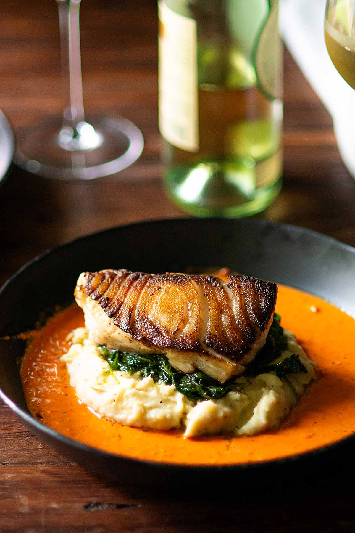 Pan Seared Chilean Sea Bass served over a bed of sautéed spinach on an island of mashed potatoes surrounded by roasted red pepper sauce.