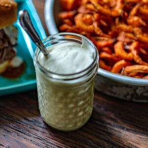 A single glass jar of homemade copycat Arby's Horsey sauce with a bowl of curly fries blurred in the background.