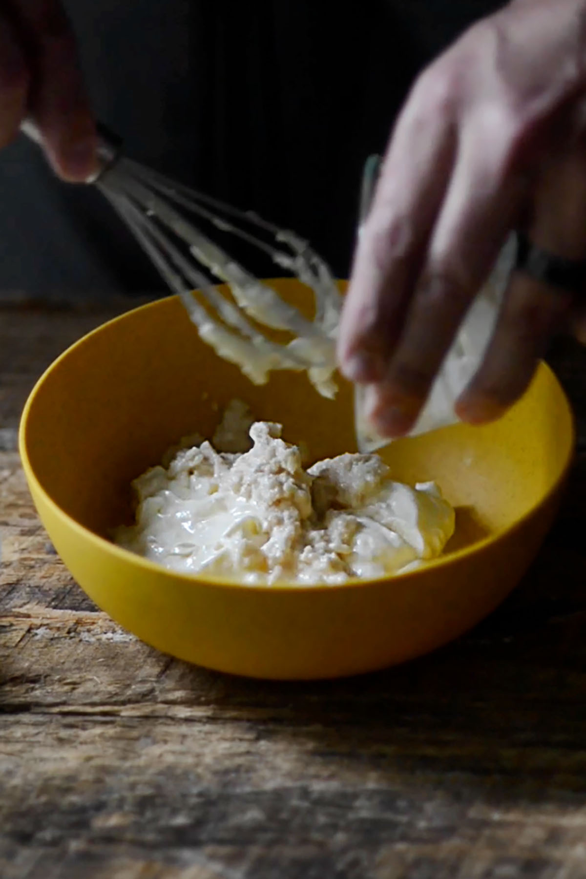 Fresh horseradish being added to a vinegar and mayonnaise mixture in a mixing bowl.