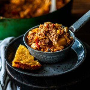 Brunswick stew served in a metal bowl on a metal plate with a side of cornbread.