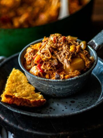 Brunswick stew served in a metal bowl on a metal plate with a side of cornbread.