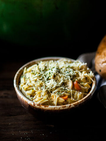 Two bowls of chicken orzo soup served with an Italian bread loaf.