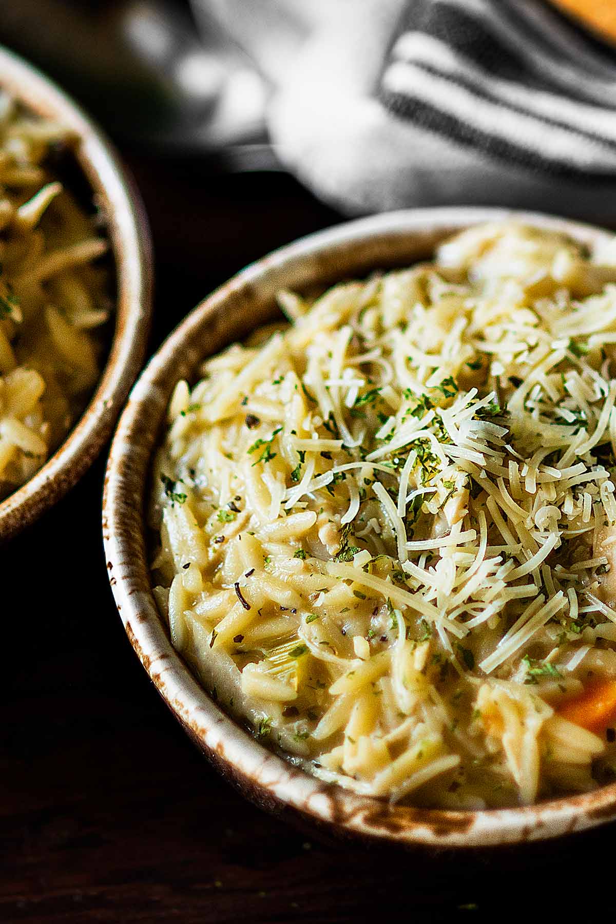 Chicken orzo soup served in rustic brown and white bowls.