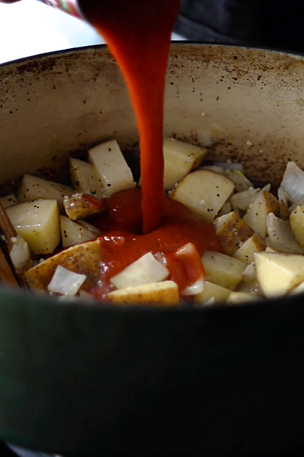 Tomato sauce being added to potatoes in a cast iron dutch oven.